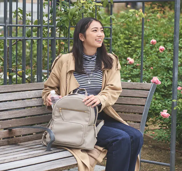 画像：女性がリュックを横に公園のベンチに座っている