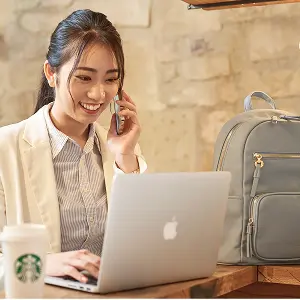 画像：カフェで女性がパソコンを開いている。リュックも置いてある。